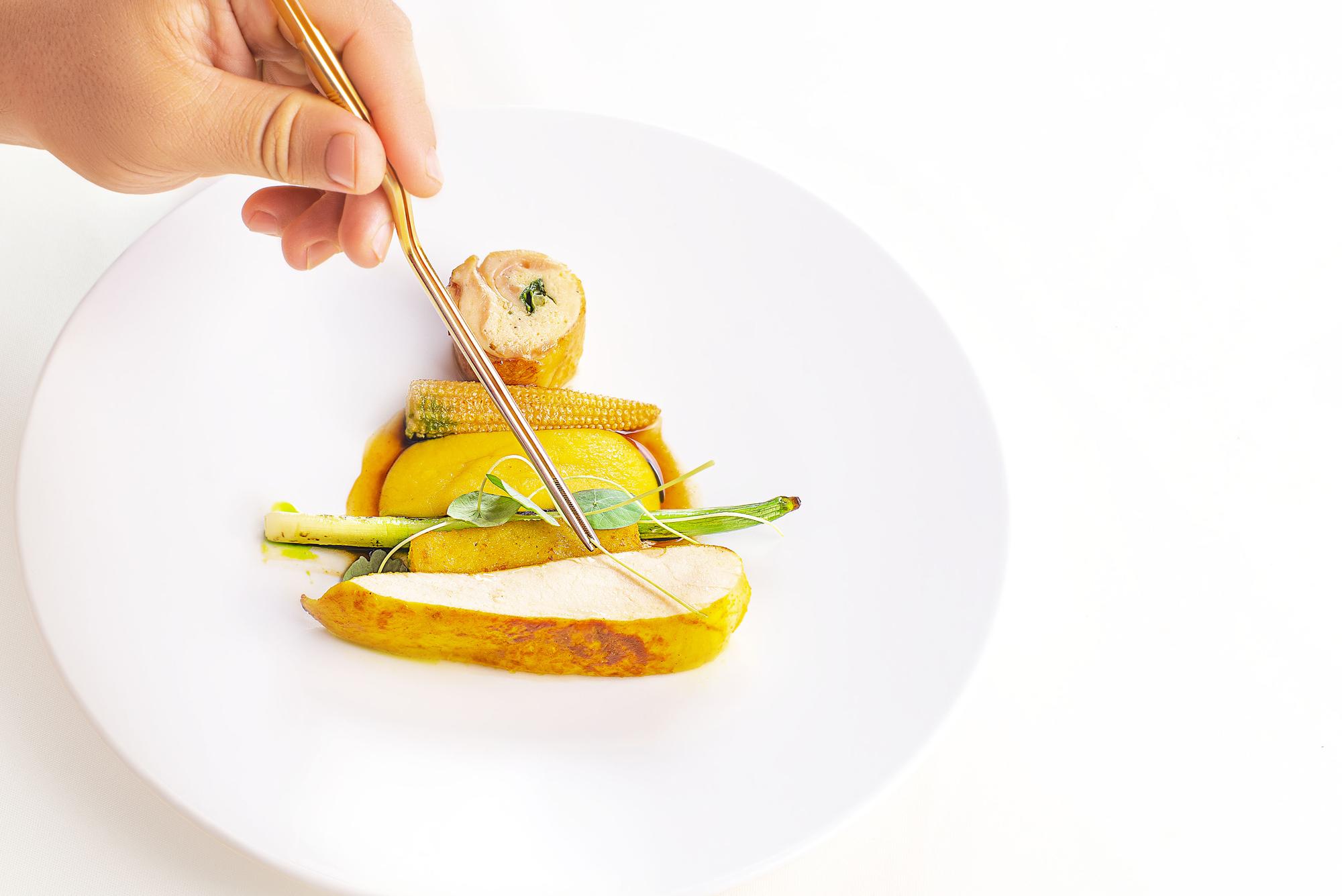 Hands plating a citrus and foam course